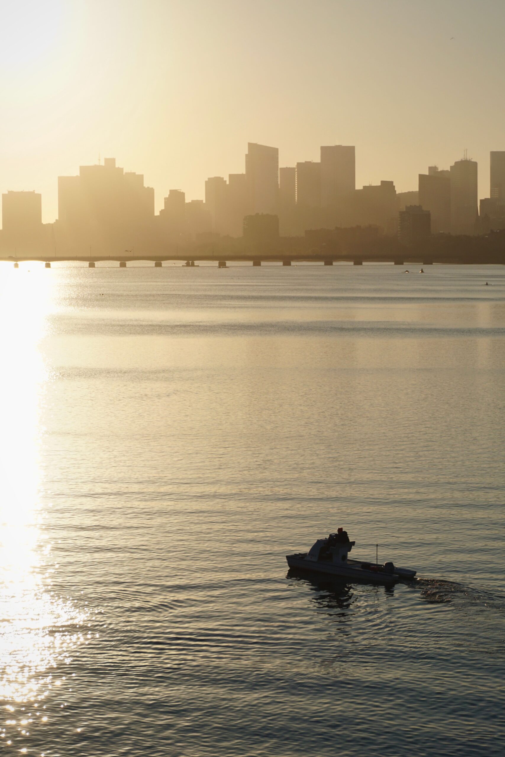 A serene silhouette of a city skyline at sunset with a small boat on calm waters.