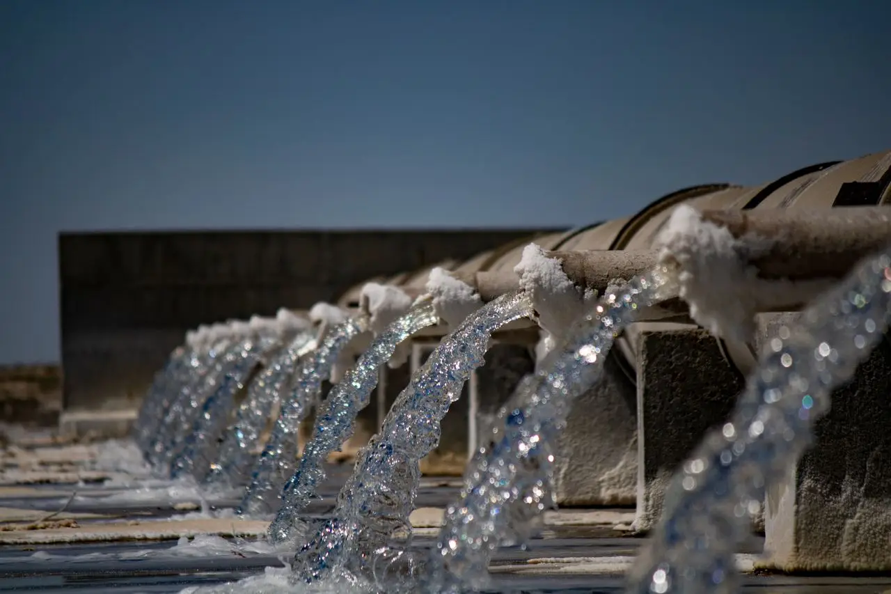 Close-up view of water flowing from industrial pipes against a clear blue sky.